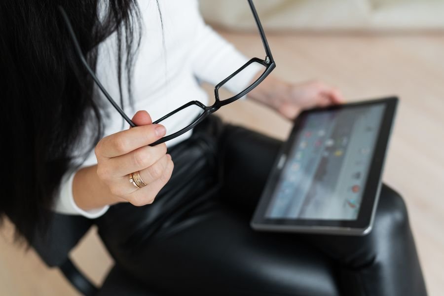 Mulher segurando óculos olhando tablet