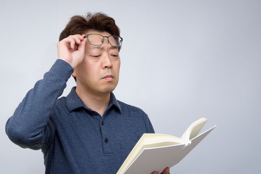 Homem levantando óculos para ler livro.
