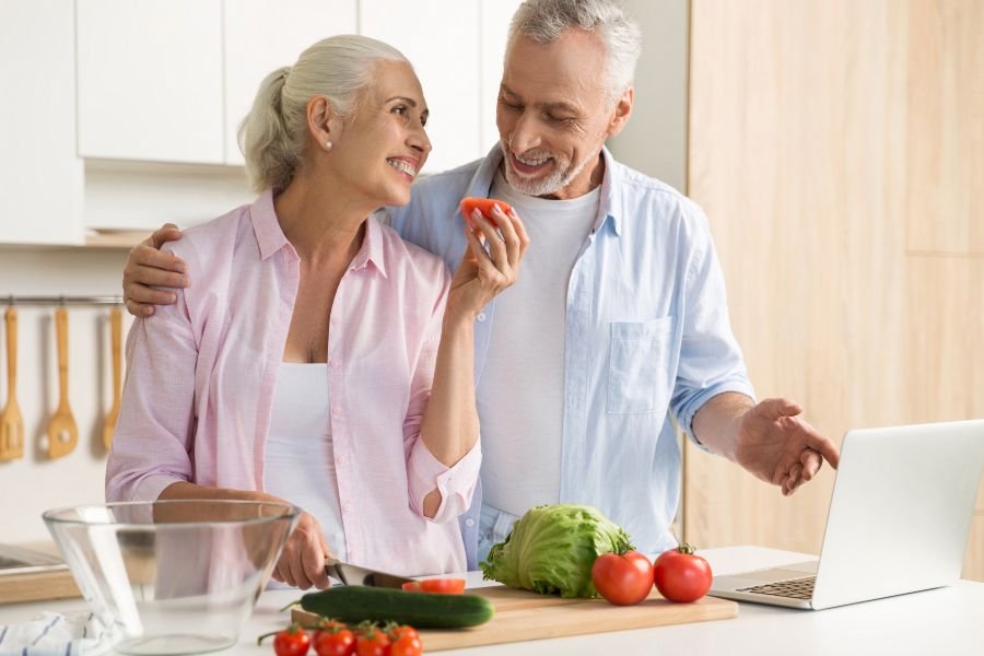 Casal de idosos sorridente cozinhando.